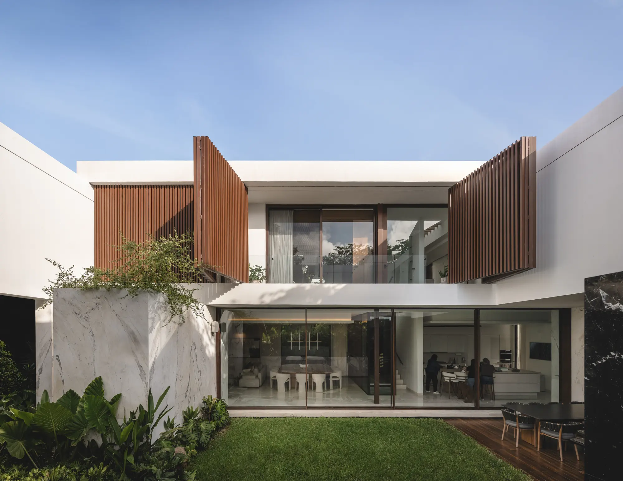 Casa RO desde el jardín: la casa en L con sala y comedor abiertos.